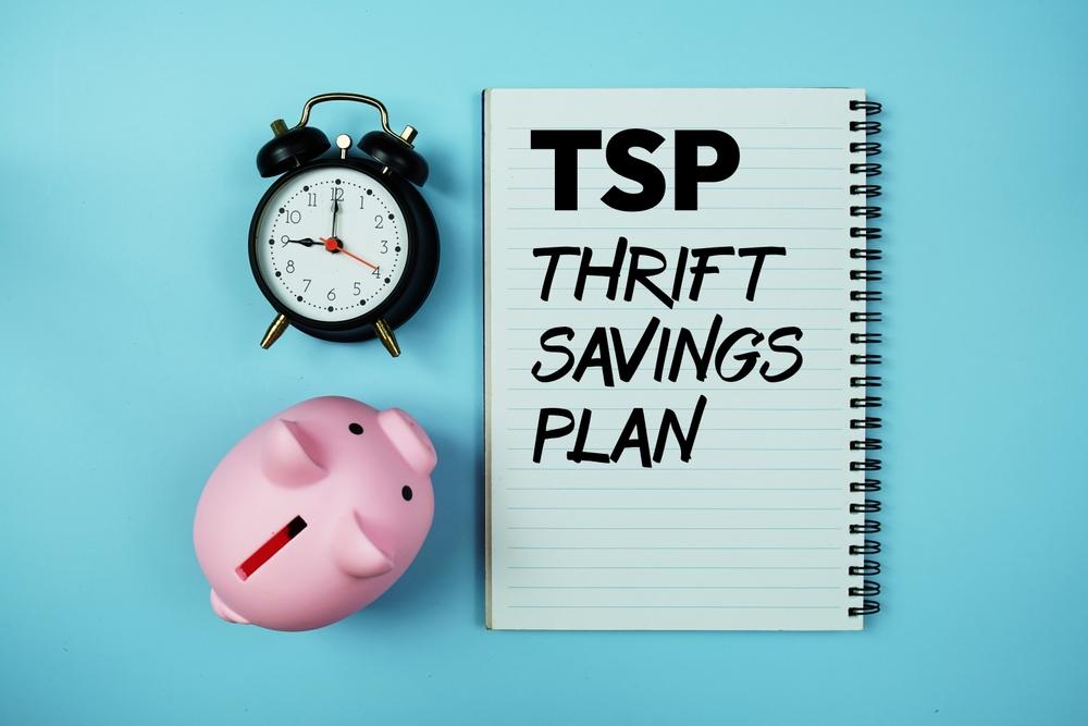 A pink piggy bank and a black alarm clock beside a notebook that reads TSP Thrift Savings Plan, on a blue background